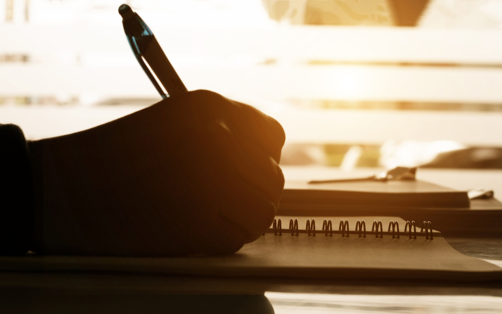 Close,up,hand,writing,notes,on,notbook,on,desk,in