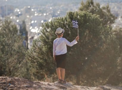 Smiling,baby,toddler,,boy,holding,a,greece,flag,on,city