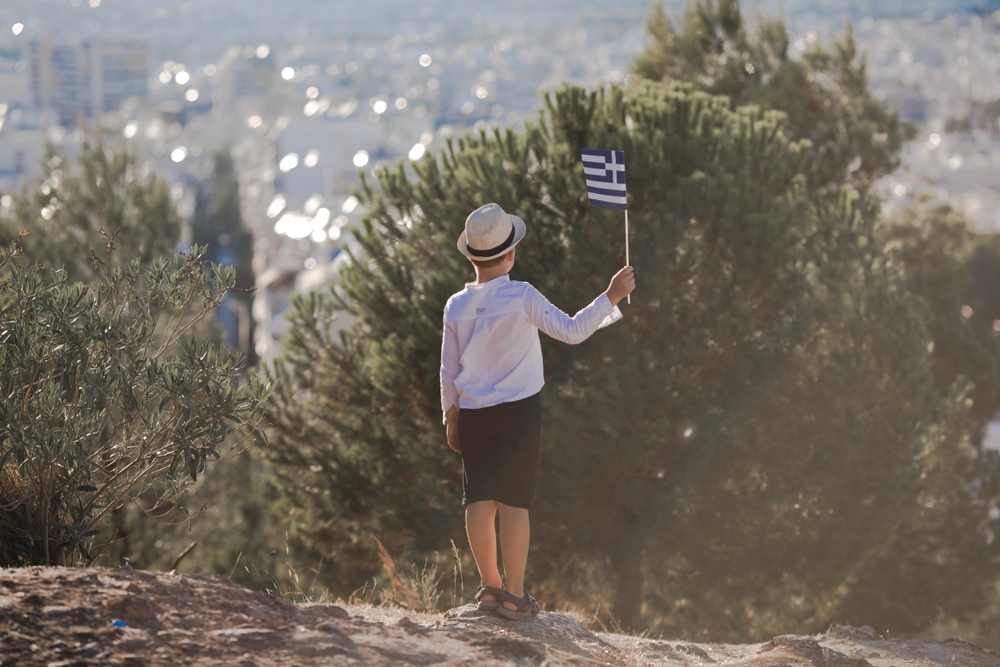 Smiling,baby,toddler,,boy,holding,a,greece,flag,on,city