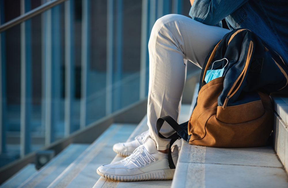 Man,with,backpack,and,face,mask,sitting,on,stairs,at
