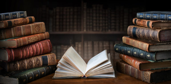 Opened,book,and,stacks,of,old,books,on,wooden,desk