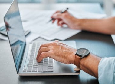 Desk,,laptop,and,hands,with,paperwork,in,office,for,bookkeeping,