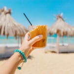 Young,woman,holding,glass,of,iced,coffee,at,the,beach
