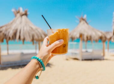 Young,woman,holding,glass,of,iced,coffee,at,the,beach