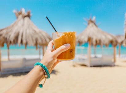 Young,woman,holding,glass,of,iced,coffee,at,the,beach