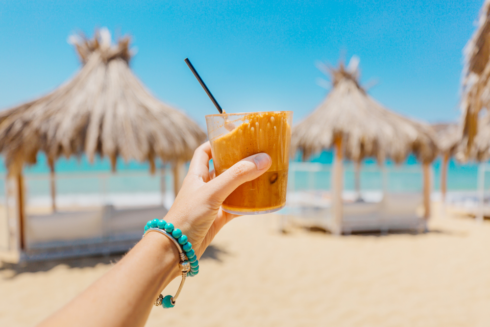 Young,woman,holding,glass,of,iced,coffee,at,the,beach