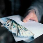 Man,hand,giving,an,envelope,full,of,euros,banknotes