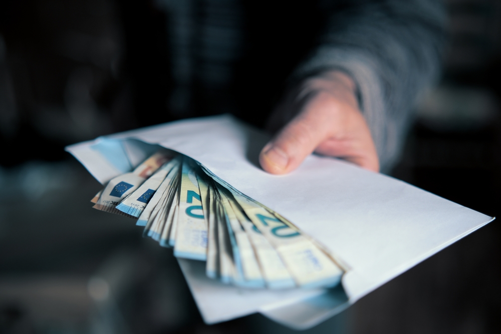 Man,hand,giving,an,envelope,full,of,euros,banknotes
