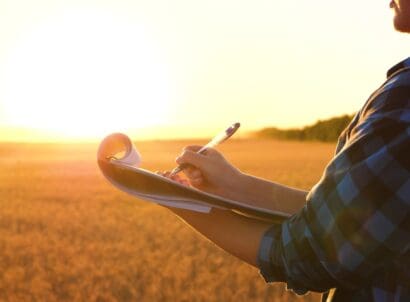 Farmer,writing,notes,in,notebook,against,golden,wheat,field ,close up
