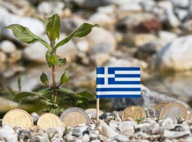 Greek,flag,with,euro,currency,coins,on,gravel,surface,business,finance,and