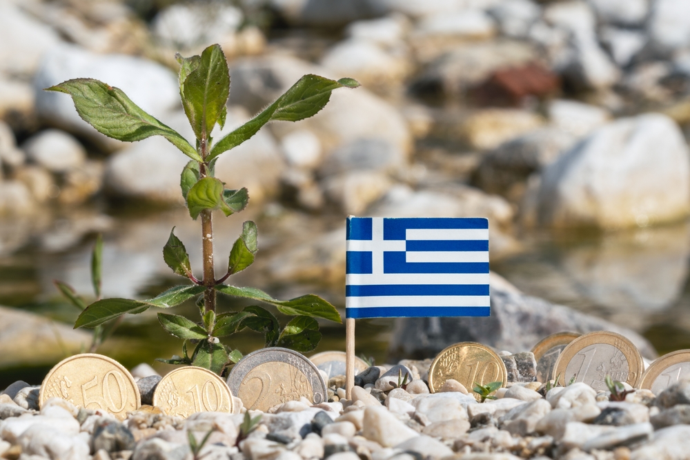 Greek,flag,with,euro,currency,coins,on,gravel,surface,business,finance,and