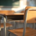 Sunlit,wooden,school,desks,and,chairs,in,an,empty,classroom,