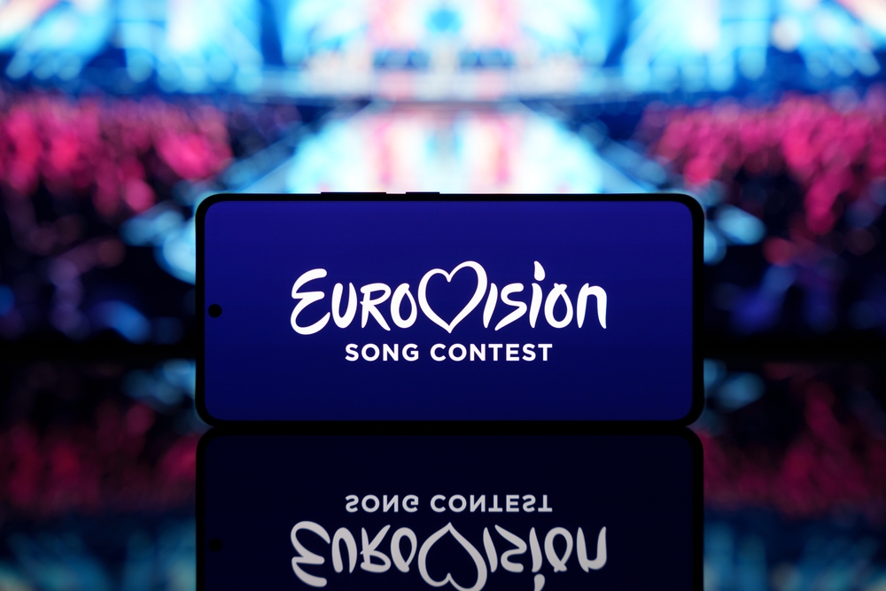 Smartphone,displaying,eurovision,song,contest,logo,with,a,blurred,stage